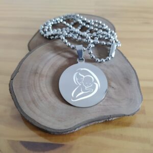 Colar Mania de Metal com pingente de mãe e bebê em fundo de madeira.