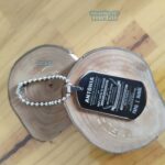 Dog Tag Grossa em Aço Inox 316L com mensagem personalizada "Antônia", ideal para presente. Plaqueta em detalhe sobre madeira rústica.