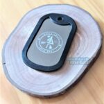 Dog Tag Fina com o logo "Delta Squad Gotas Army" em base de madeira.