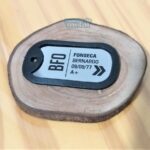 Dog tag colorida personalizada com nome, data e tipo sanguíneo sobre base de madeira.