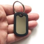 Chaveiro Dog Tag Fina mono na mão. Placa de identificação com borda preta.