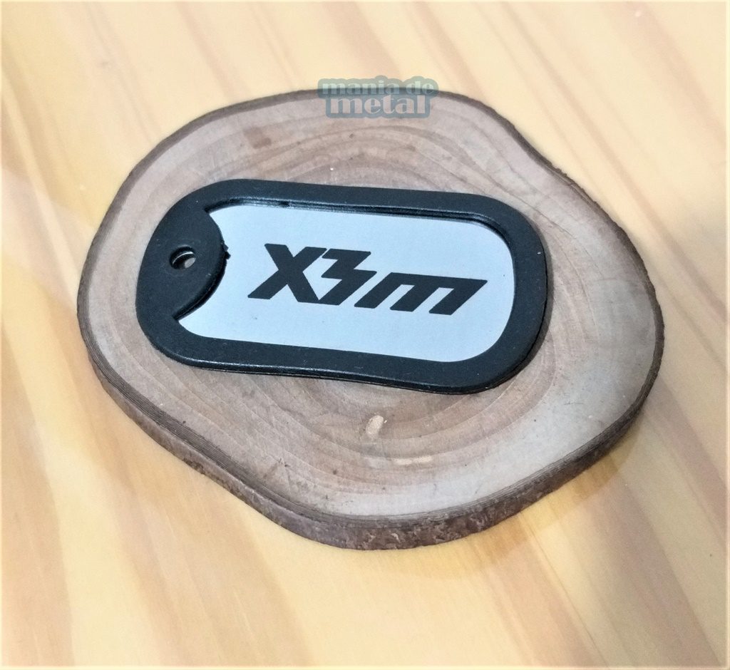 Dog tag color prata com borda preta e a inscrição "X3m".