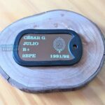 Dog Tag Fina com nome César G. Julio, tipo sanguíneo B+, e brasão do Brasil em base de madeira.