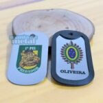 Dog tags coloridos com emblemas militares brasileiros. Um com "1º PEL PREDADOR" e outro com "OLIVEIRA".