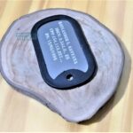 Dog Tag Fina preta com dados pessoais gravados sobre base de madeira rústica.